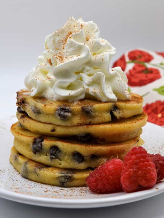 A plated stack of Cannoli Pancakes topped with whipped cream and raspberries on the side